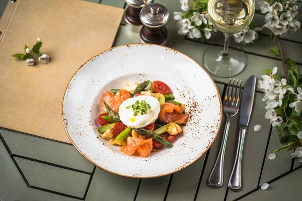 Steamed vegetables with salmon slices and egg pashot on top served on plate on setting table