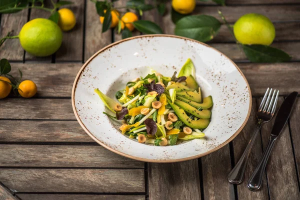 Fresh salad with avocado and nuts in plate on wooden table