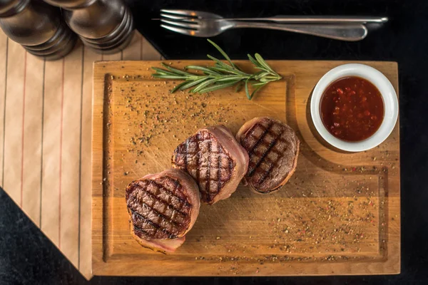 Grilled beef sirloin steaks served on wooden board with sauce