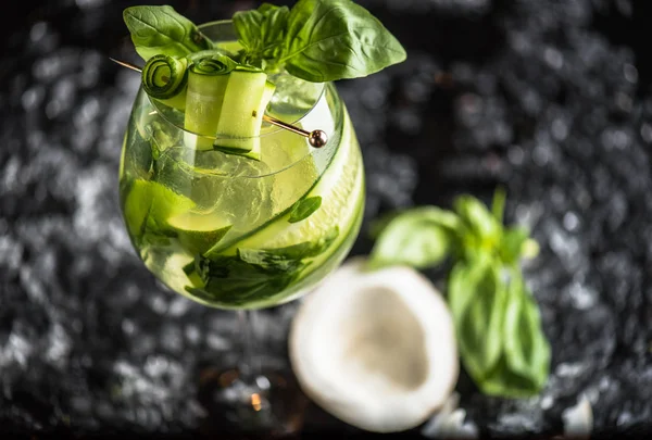 Cocktail with basil, lime and coconut in glass on dark background with ice