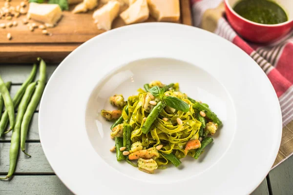 Italian vegetable pasta with pesto sauce served on plate on wooden table with ingredients