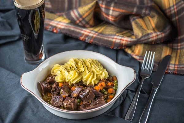 Braised meat in gravy with mushed potato on plate on fabric