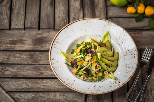 Fresh salad with avocado and nuts in plate on wooden table