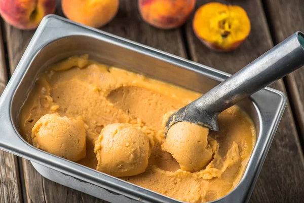 Peach ice cream in container with spoon on wooden table