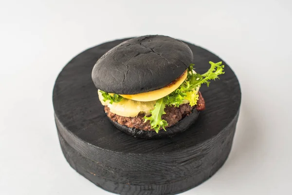 Black beef burger served on piece of wood on white background