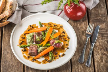 Havuç ile sığır eti ve ahşap masa üzerinde sunulan beyaz tabakta sos