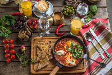 shakshuka, zeytin, biber, domates, ekmek, meyve suyu ve kahve rustik ahşap tablo ile kahvaltı