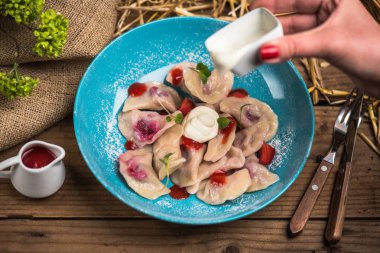 Mavi tabakta insan eli dökme ekşi krema çilek ve reçel ile tatlı köfte üzerinde