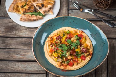 Ev yapımı humus ahşap masa üzerinde kase taze sebze ile süslenmiş