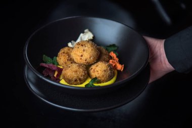 karanlık arka planda sos ile kızarmış mozzarella topları insan eli tutan kase