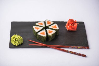 geleneksel gurme Japon üçgen suşi somon, yemek çubukları, zencefil ve gri arka plan üzerinde kayrak gemide wasabi ile