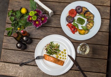 Parça somon, salata ve plakaları kadeh beyaz şarap ile ahşap masa üzerinde ızgara sebzeler ile akşam yemeği
