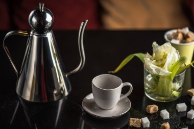 Siyah arka plan üzerinde fincan, çiçek ve kahverengi ve beyaz şeker küpleri ile Çaydanlık