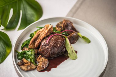 Beyaz tabak içinde kavrulmuş et mantar ve ıspanak ile servis