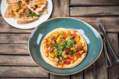 Ev yapımı humus ahşap masa üzerinde kase taze sebze ile süslenmiş