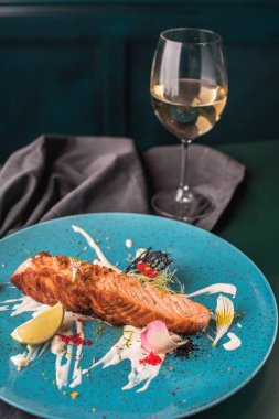 Ahşap masa üzerinde mavi plaka üzerinde sos ve yenilebilir çiçekler ile Somon kızarmış parça