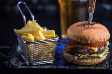 Sığır eti burger tepside koyu arka plan üzerinde kızarmış patates dilimleri ile servis