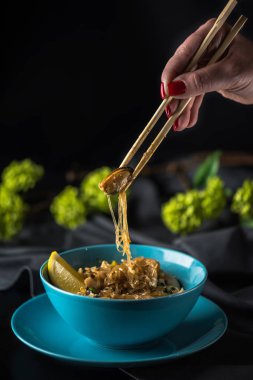 Çubuk üzerinde kase Asya deniz ürünleri erişte koyu arka plan üzerinde tutan el