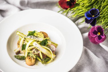 Kumaş üzerine beyaz tabakta kavrulmuş tarak taze sebze ile servis