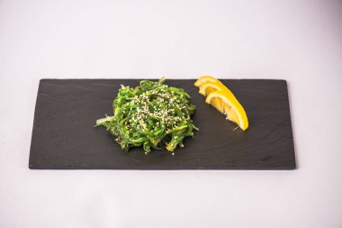 Beyaz zemin üzerine limon dilimleri ile kayrak üzerinde yosun salata servis