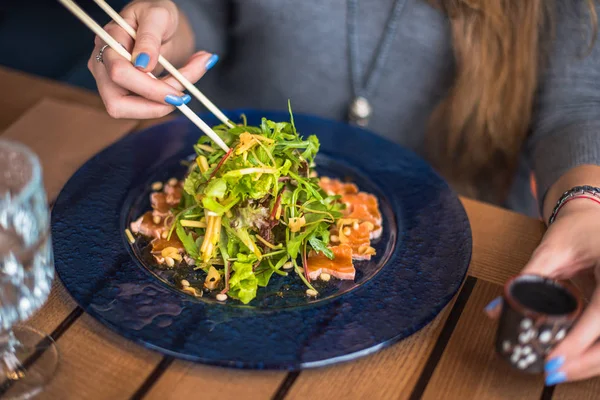 close-up of woman eating fish sashimi and salad with chopsticks