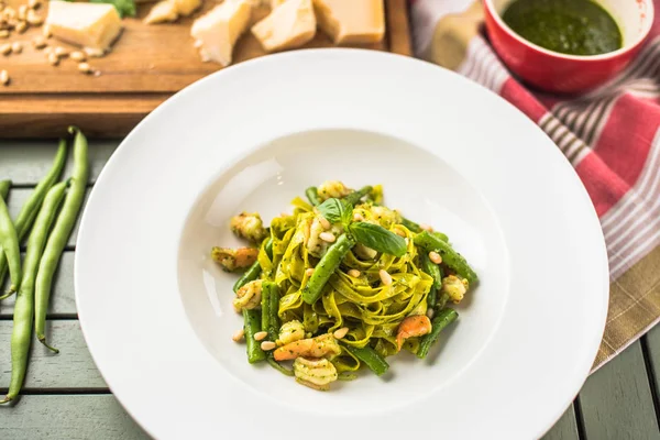 Italian vegetable pasta with pesto sauce served on plate on wooden table with ingredients