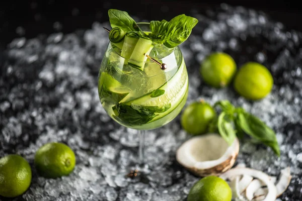 Cocktail in glass, coconut, lime, cucumber on ice on dark background. Drink of fresh lemonade close-up