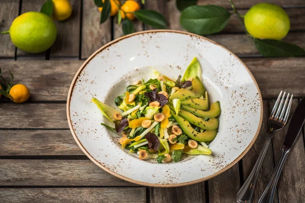 Fresh salad with avocado and nuts in plate on wooden table