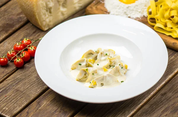 Traditional italian spinach ravioli in cream sauce served on white plate on wooden table with ingredients