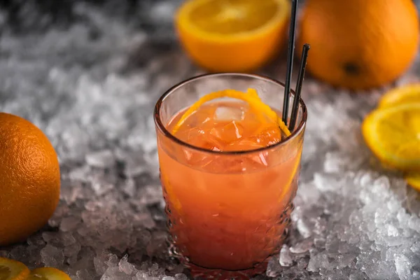 Orange cocktail in glass on ice with ingredients