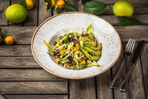 Fresh salad with avocado and nuts in plate on wooden table