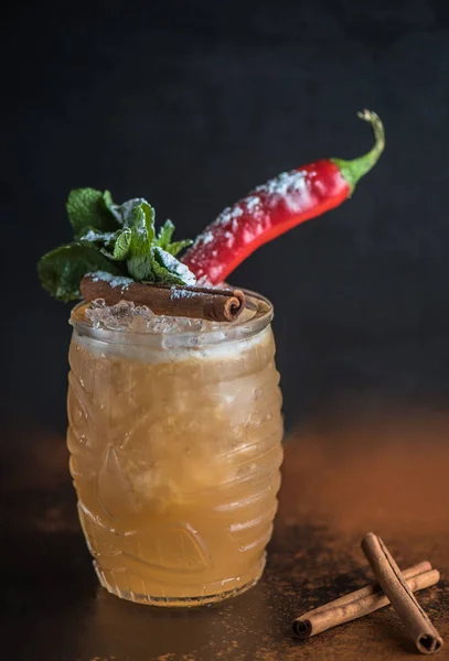 Cocktail in glass with cinnamon sticks and chilly pepper on brown background