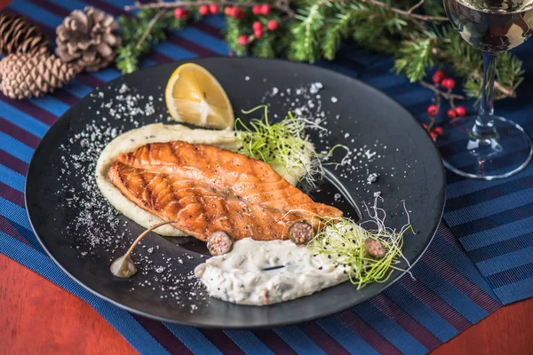 Grilled salmon piece with sauce and lemon served on plate on background of christmas decor