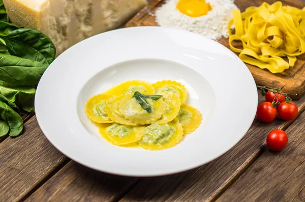 Traditional italian spinach ravioli served on white plate on wooden table with ingredients