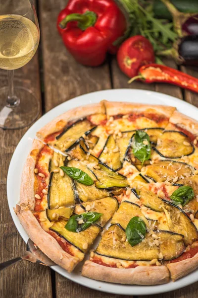 Baked vegetable pizza with aubergine and pine nuts on plate on wooden table