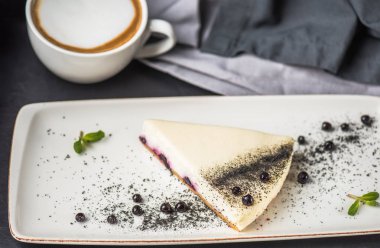 Berry cheesecake beyaz plaka üzerinde parça fincan kapuçino üzerinde gri masa örtüsü ile 