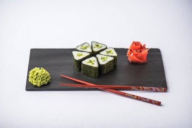 zencefil, wasabi ve gri arka plan üzerinde kayrak gemide yemek çubukları ile gurme üçgen suşi