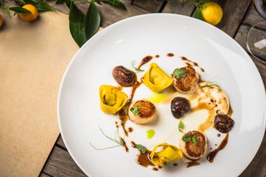 Yaprakları ile ahşap masa üzerinde beyaz tabakta Ravioli tarak ve sos ile servis