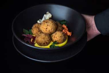 karanlık arka planda sos ile kızarmış mozzarella topları insan eli tutan kase