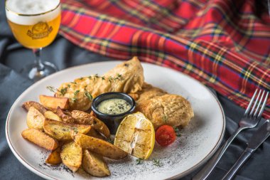 Kızarmış balık ve patates bardak bira ile kumaş üzerine plaka üzerinde sos ile 