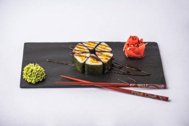 geleneksel gurme Japon üçgen suşi yemek çubukları, zencefil ve gri arka plan üzerinde kayrak gemide wasabi