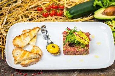 Taze tartar malzemeler ve arka plan üzerinde saman ile çiğ yumurta sarısı ve ekmek parçaları ile beyaz tabakta servis