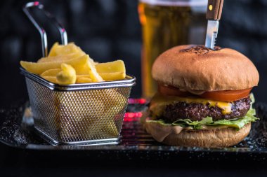 Sığır eti burger tepside koyu arka plan üzerinde kızarmış patates dilimleri ile servis