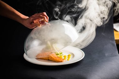 insan eli ile Somon parça ve siyah arka plan üzerine sebze salatası yemek üzerinden şeffaf kapak kaldırma 