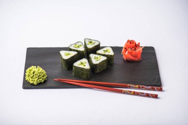 zencefil, wasabi ve gri arka plan üzerinde kayrak gemide yemek çubukları ile geleneksel üçgen suşi