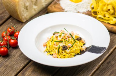 Ahşap masa üzerinde beyaz tabakta servis deniz ürünleri makarna