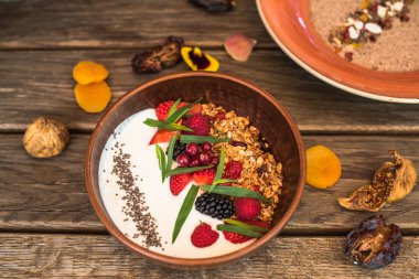 Kahvaltı yoğurt, granola ve çiçekli tahta masada kase çilek ile