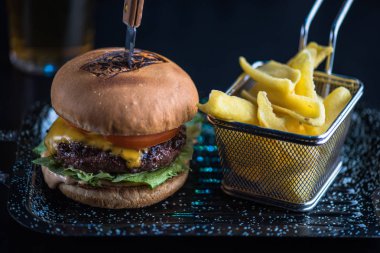 Sığır eti burger tepside koyu arka plan üzerinde kızarmış patates dilimleri ile servis