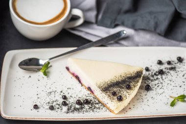 Berry cheesecake beyaz plaka üzerinde parça fincan kapuçino üzerinde gri masa örtüsü ile 