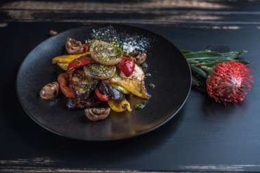 Izgara sebze çiçek ile ahşap masa üzerinde siyah plaka üzerinde devam eder